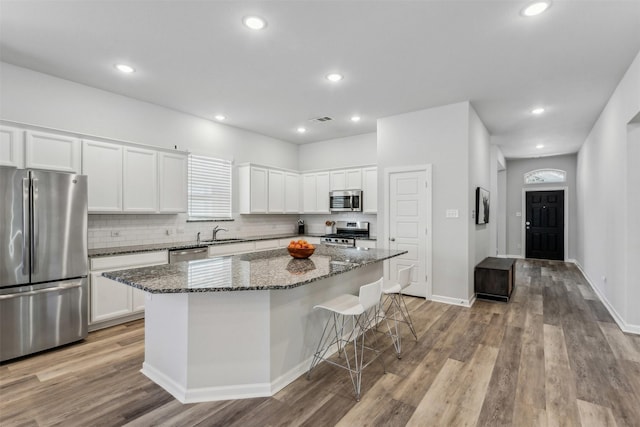 kitchen featuring dark stone countertops, stainless steel appliances, a kitchen island, and white cabinets