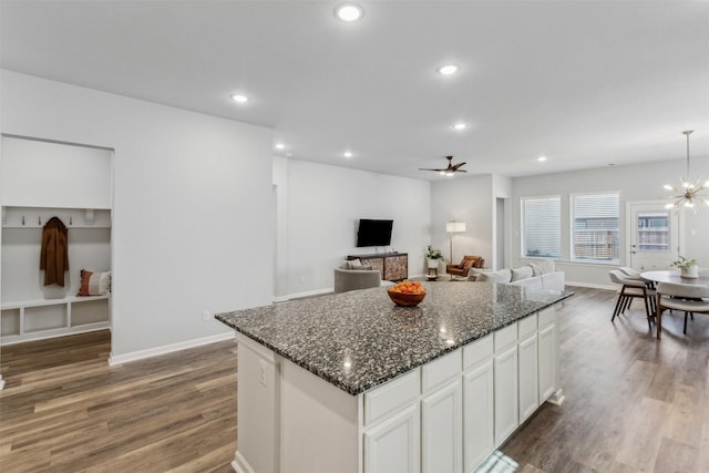 kitchen with dark wood-type flooring, white cabinetry, a kitchen island, dark stone counters, and ceiling fan with notable chandelier