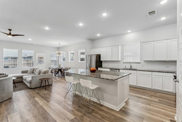 kitchen with appliances with stainless steel finishes, hanging light fixtures, white cabinets, a kitchen island, and dark stone counters