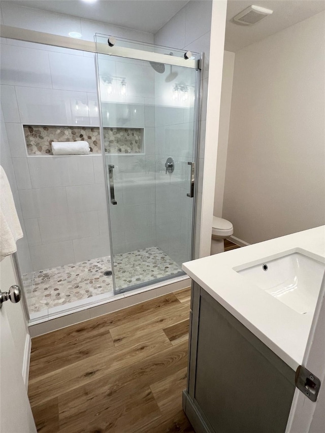 bathroom featuring hardwood / wood-style flooring, vanity, a shower with shower door, and toilet