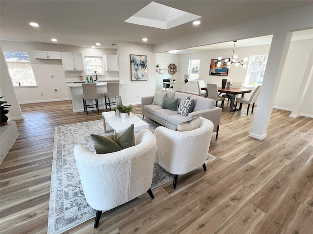 living room with a healthy amount of sunlight, sink, an inviting chandelier, and light hardwood / wood-style flooring