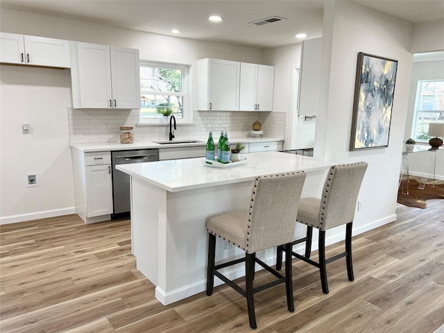 kitchen featuring light wood-type flooring, stainless steel dishwasher, sink, and white cabinets