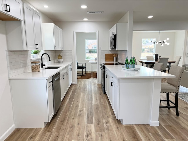 kitchen featuring appliances with stainless steel finishes, pendant lighting, sink, white cabinets, and light hardwood / wood-style flooring