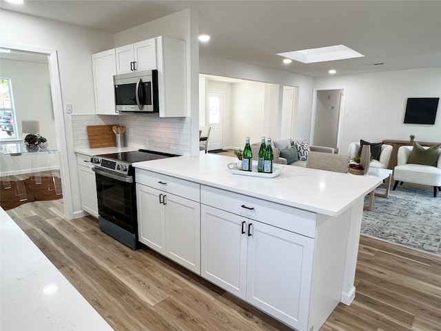 kitchen featuring a skylight, tasteful backsplash, white cabinetry, stainless steel appliances, and light wood-type flooring