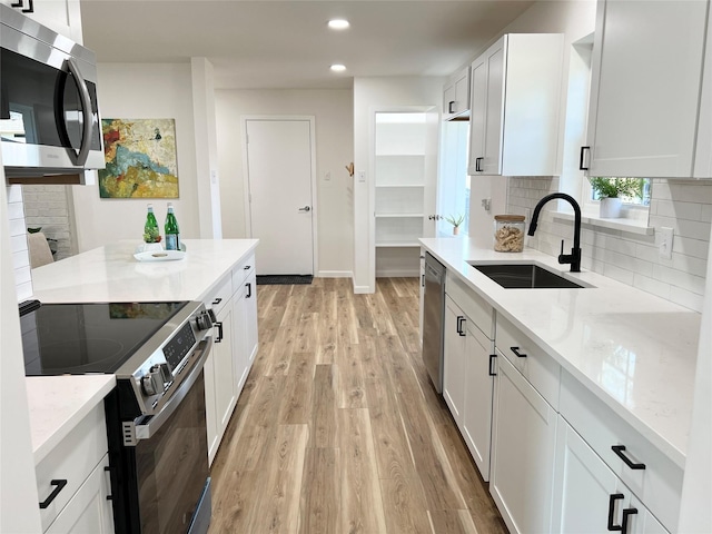 kitchen featuring stainless steel appliances, light stone countertops, sink, and white cabinets