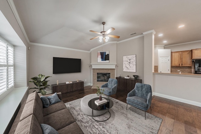 living room with vaulted ceiling, dark hardwood / wood-style flooring, a tiled fireplace, ornamental molding, and ceiling fan