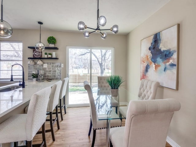 dining space with an inviting chandelier, sink, and light wood-type flooring