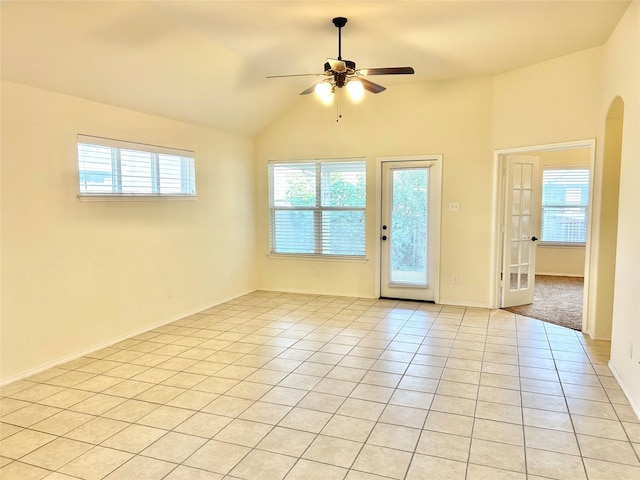 empty room featuring ceiling fan, plenty of natural light, vaulted ceiling, and light tile patterned flooring