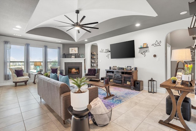 living area with light tile patterned floors, baseboards, arched walkways, a ceiling fan, and a fireplace