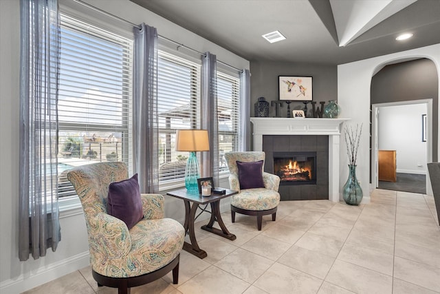 living area with arched walkways, light tile patterned floors, visible vents, a tile fireplace, and baseboards