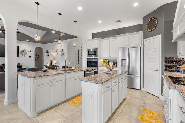 kitchen featuring an island with sink, white cabinetry, arched walkways, and stainless steel appliances