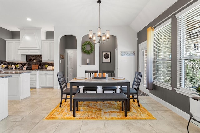 dining room with light tile patterned floors, baseboards, a chandelier, and arched walkways