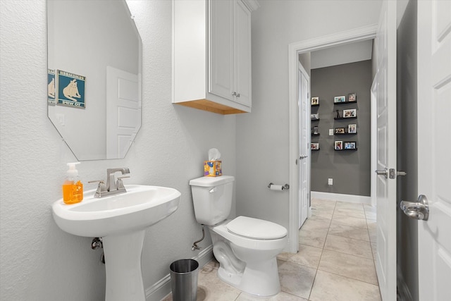 half bathroom with a sink, toilet, baseboards, and tile patterned floors