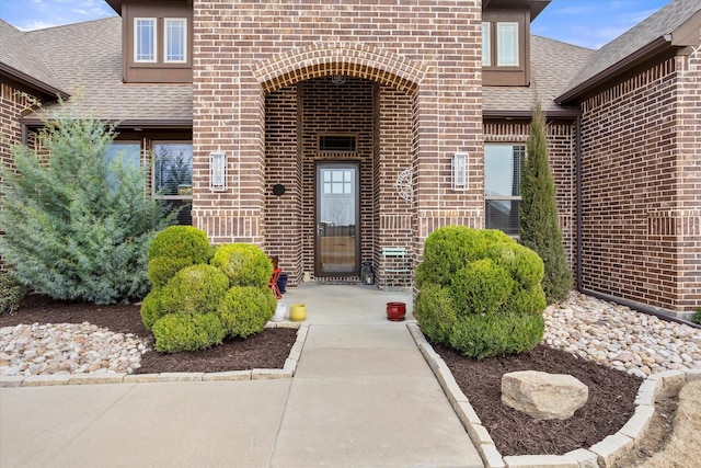 doorway to property featuring a shingled roof and brick siding