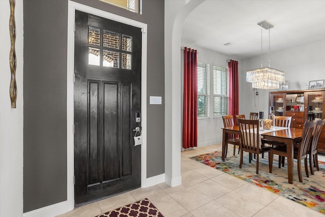 entryway featuring baseboards, arched walkways, a chandelier, and light tile patterned flooring