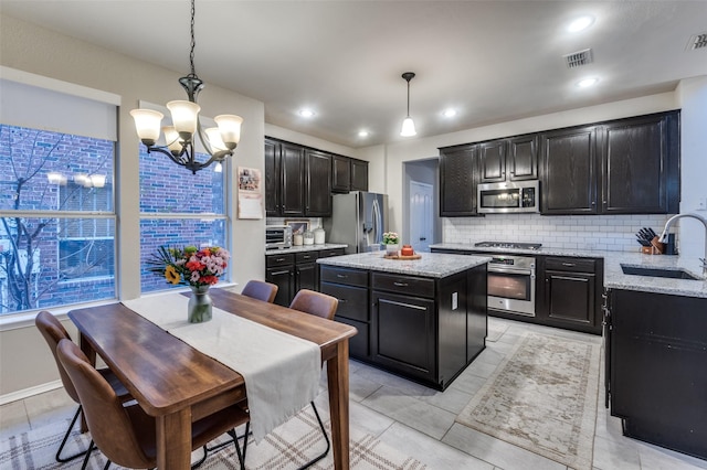 kitchen with appliances with stainless steel finishes, sink, light stone counters, and decorative light fixtures