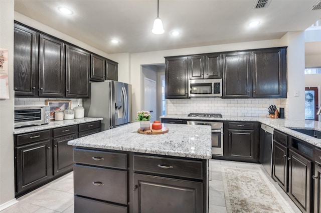 kitchen with decorative light fixtures, appliances with stainless steel finishes, a kitchen island, light stone countertops, and backsplash