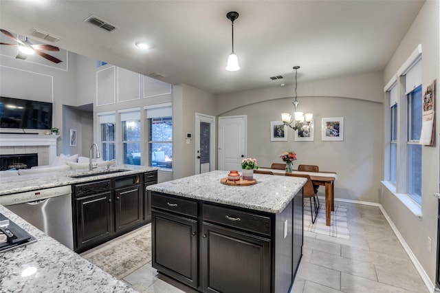 kitchen with sink, light stone counters, hanging light fixtures, stainless steel dishwasher, and a kitchen island