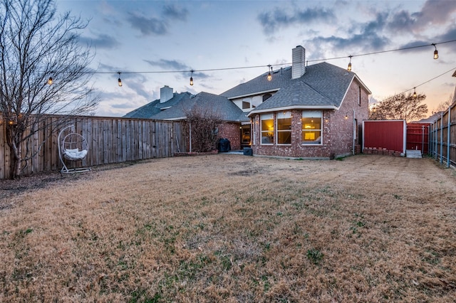 back house at dusk featuring a lawn