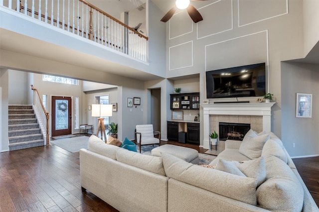 living room with ceiling fan, a fireplace, dark hardwood / wood-style flooring, and a towering ceiling