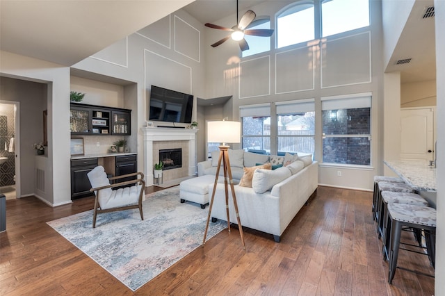 living room with a tiled fireplace, dark hardwood / wood-style floors, and ceiling fan