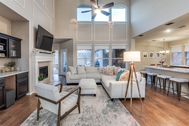 living room with dark hardwood / wood-style flooring, sink, ceiling fan with notable chandelier, and a fireplace