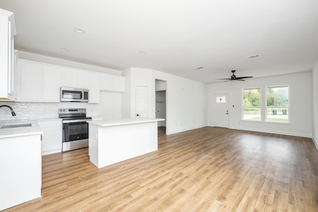 kitchen featuring sink, appliances with stainless steel finishes, white cabinets, a kitchen island, and light wood-type flooring