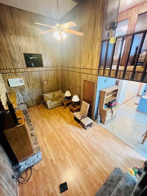 living room featuring ceiling fan, wood-type flooring, and wooden walls