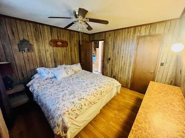 bedroom featuring ornamental molding, hardwood / wood-style floors, ceiling fan, and wooden walls