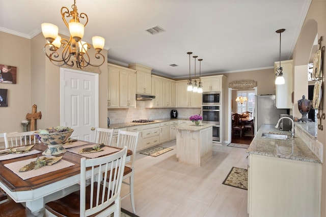 kitchen featuring appliances with stainless steel finishes, a center island, an inviting chandelier, cream cabinets, and a sink