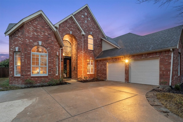 traditional-style house featuring a garage, brick siding, roof with shingles, and driveway