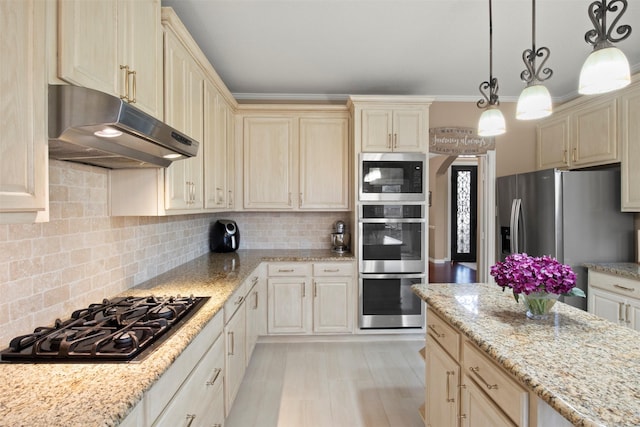 kitchen with backsplash, under cabinet range hood, pendant lighting, cream cabinets, and stainless steel appliances