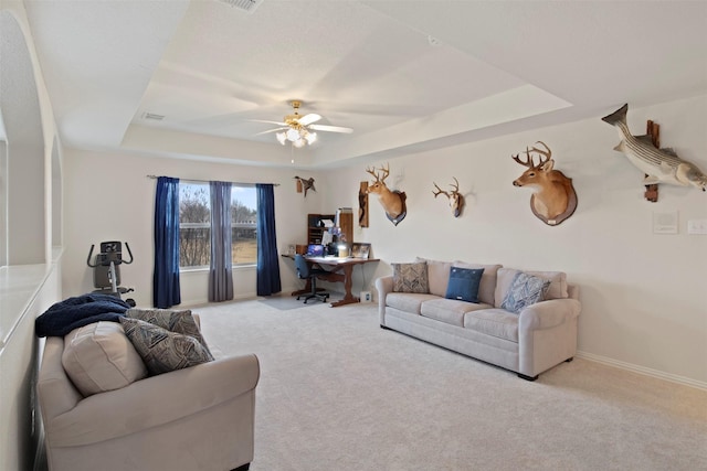 carpeted living area featuring a raised ceiling, visible vents, baseboards, and ceiling fan