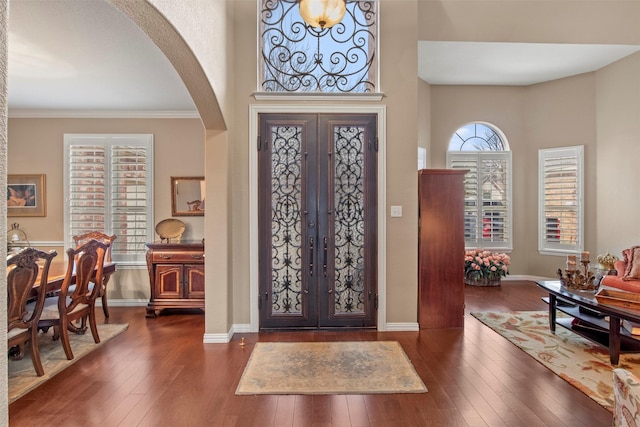 entrance foyer with hardwood / wood-style floors, baseboards, arched walkways, french doors, and crown molding