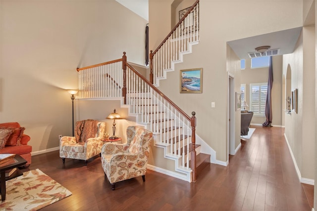 stairway with visible vents, baseboards, a towering ceiling, hardwood / wood-style flooring, and arched walkways