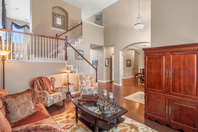 living area featuring arched walkways, stairway, baseboards, and wood finished floors