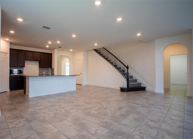 kitchen featuring sink, decorative backsplash, dark brown cabinets, and a center island with sink