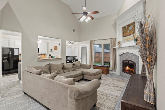 living room featuring high vaulted ceiling, a premium fireplace, visible vents, a ceiling fan, and light wood-style floors