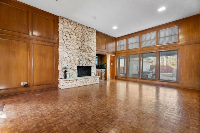 unfurnished living room featuring a fireplace, wooden walls, parquet floors, and a textured ceiling