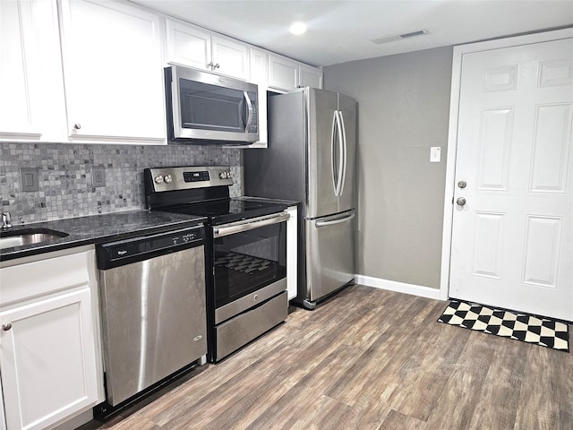 kitchen with white cabinetry, dark stone countertops, stainless steel appliances, dark hardwood / wood-style floors, and tasteful backsplash