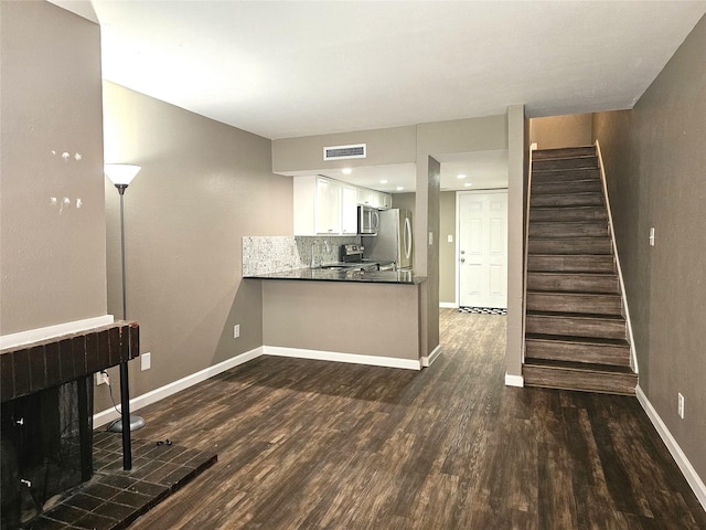 kitchen with dark wood-type flooring, appliances with stainless steel finishes, kitchen peninsula, decorative backsplash, and white cabinets