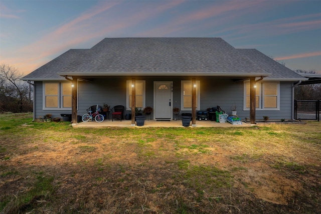 back house at dusk with a patio area and a lawn