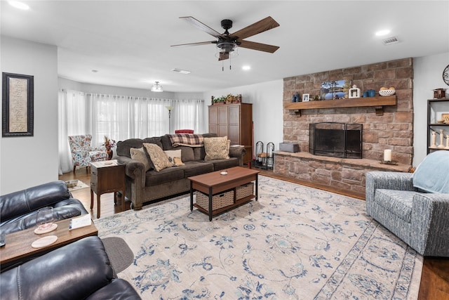 living room featuring ceiling fan, wood-type flooring, and a stone fireplace