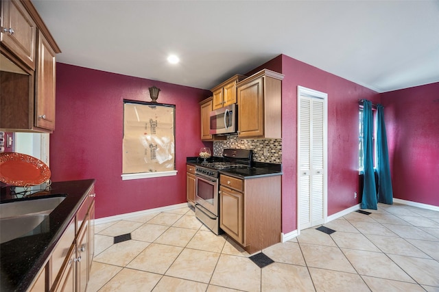 kitchen with light tile patterned floors, sink, dark stone countertops, stainless steel appliances, and decorative backsplash