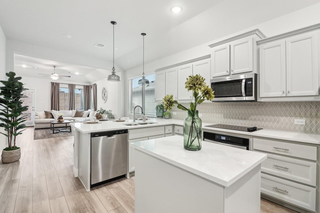 kitchen featuring appliances with stainless steel finishes, open floor plan, decorative light fixtures, light countertops, and a sink