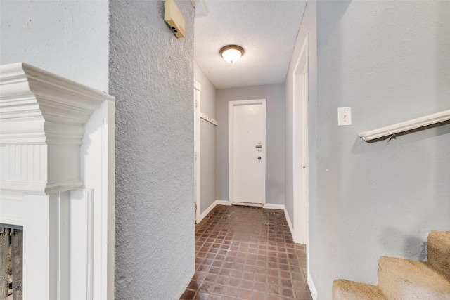 hallway featuring stairs, baseboards, a textured ceiling, and a textured wall