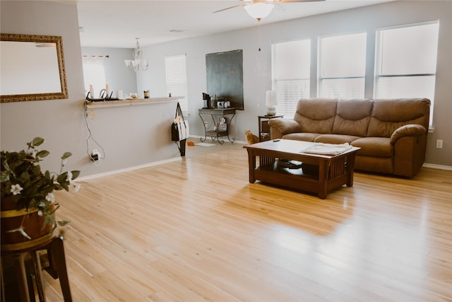 living room featuring ceiling fan with notable chandelier, light wood-style floors, and baseboards