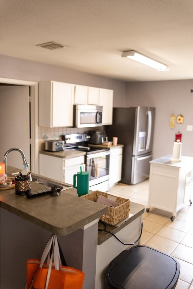 kitchen featuring light tile patterned flooring, appliances with stainless steel finishes, sink, white cabinets, and backsplash