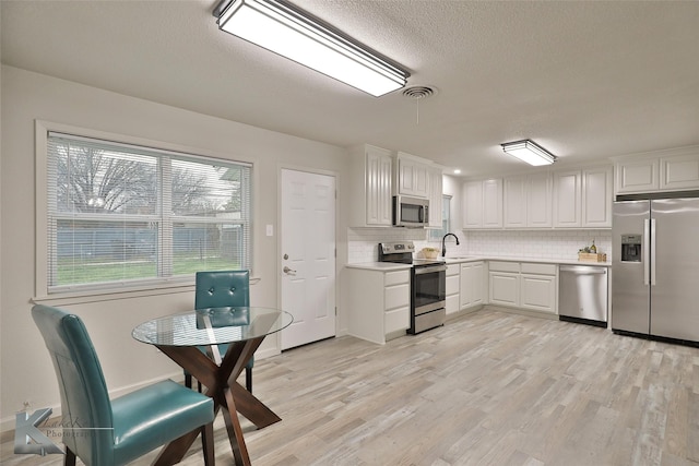 kitchen with white cabinetry, appliances with stainless steel finishes, light wood-type flooring, and backsplash