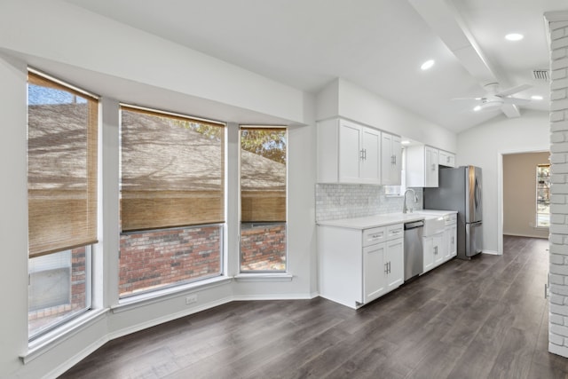 kitchen featuring dark wood-type flooring, white cabinetry, lofted ceiling with beams, appliances with stainless steel finishes, and backsplash